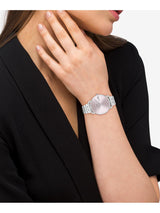 A silver-tone women's watch with a round dial and matching metal link bracelet, shown worn on a model's wrist. The model is wearing a black blazer against a clean white background.