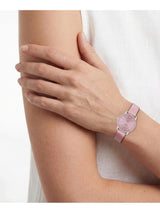 A close-up of a model's arm and hand wearing a slim pink watch with a silver-toned bezel and matching pink strap.