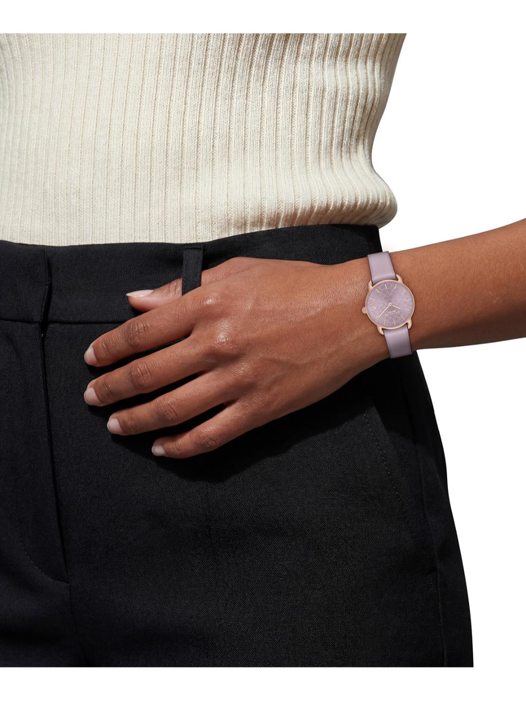 A close-up of a person's hand resting on black trousers, wearing a light pink watch with a matching pink strap and rose gold-toned case.