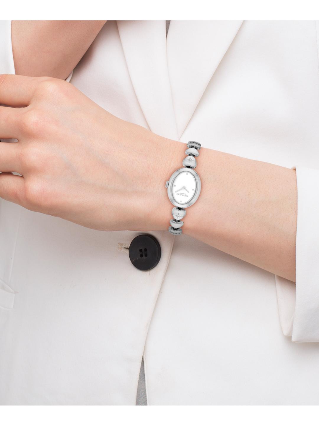 A silver-toned beaded bracelet watch with an oval white dial, shown worn on a person's wrist. The person is wearing a white blazer.