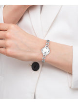 A silver-tone women's watch with a white dial and a distinctive segmented link bracelet, shown worn on a person's wrist. The person is wearing a white blazer, and the watch is positioned over the white button of the blazer.