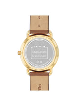 The back view of a Coach wristwatch with a gold-tone case and a brown leather strap, showing the brand name and technical specifications on the crystal.