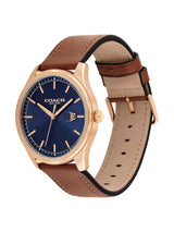 A Coach New York wristwatch with a rose gold case, a textured navy blue dial, and a brown leather strap with a tan interior, shown on a plain white background.