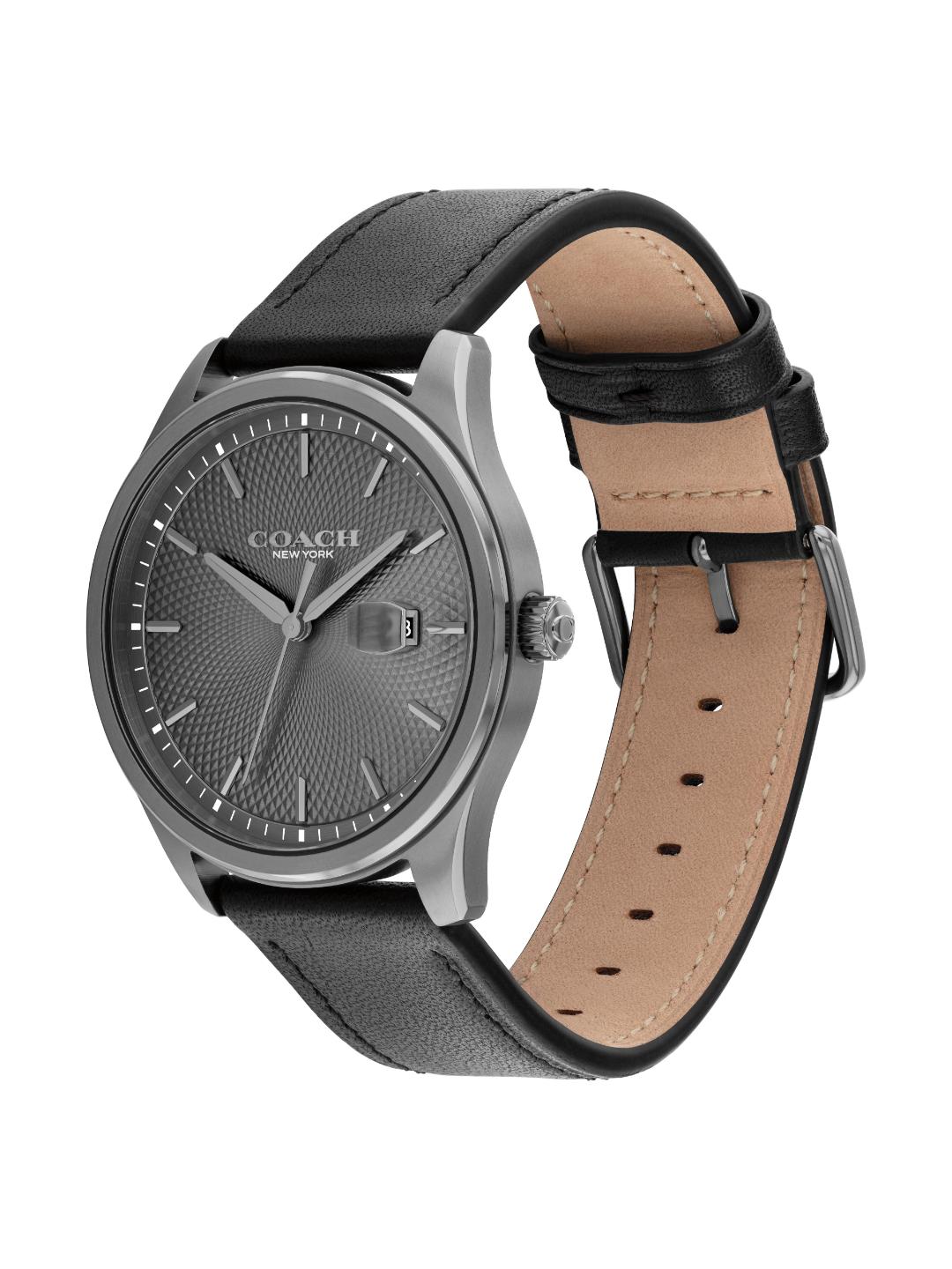 A Coach New York wristwatch with a textured dark gray dial, a silver-tone case, and a black leather strap with a tan interior, shown on a plain white background.