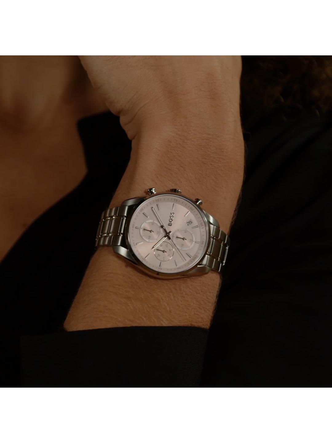 A silver-toned metal link watch with a white dial and chronograph subdials, shown worn on a person's wrist against a dark background.