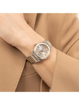 A two-tone stainless steel and gold watch with a silver dial, worn on a person's wrist dressed in a tan blazer.