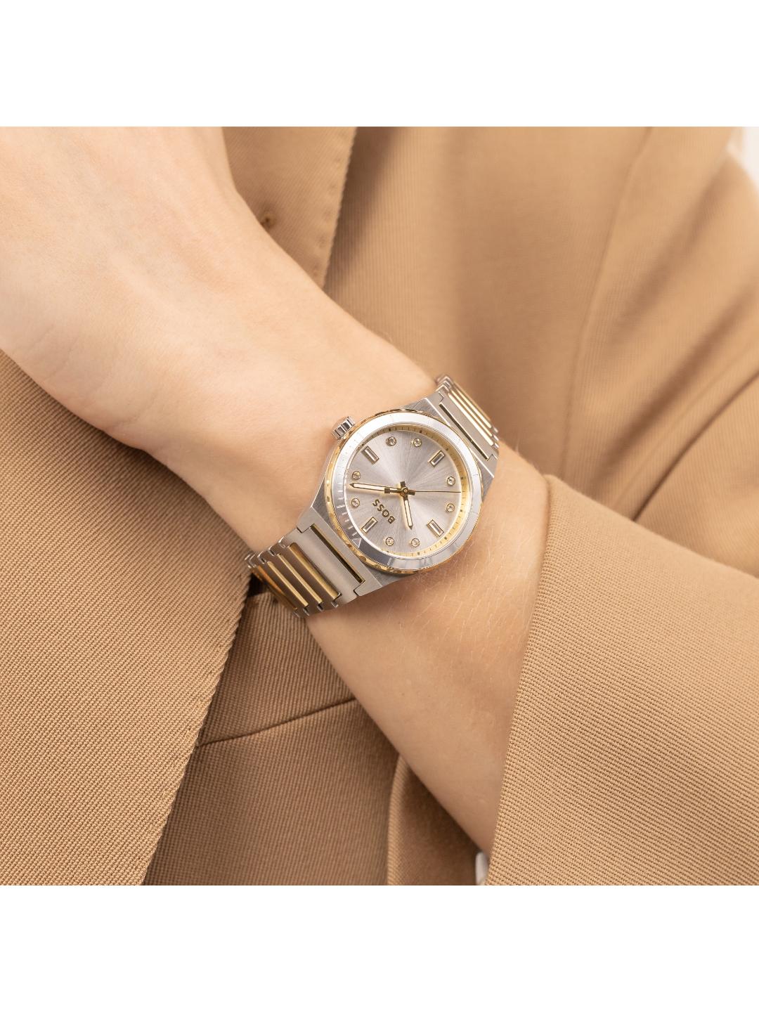 A two-tone stainless steel and gold watch with a silver dial, worn on a person's wrist dressed in a tan blazer.