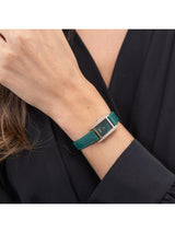 A close-up of a woman's wrist wearing a green leather watch strap with a silver-toned metal buckle and bezel.
