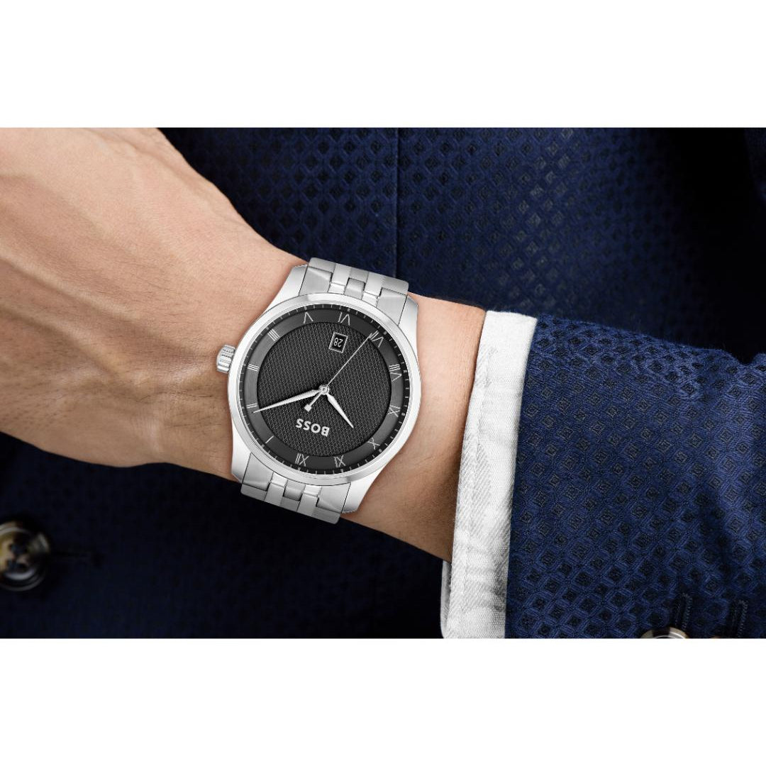 A silver stainless steel wristwatch with a black dial and date window, worn on a person's wrist. The person is wearing a textured navy blue suit jacket and a white collared shirt cuff.