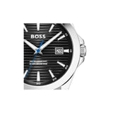 A close-up of a Hugo Boss wristwatch with a black dial, silver-tone stainless steel case, silver-tone hour markers, and a blue seconds hand on a white background.