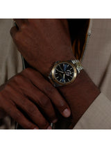 A close-up of a man's wrist wearing a two-tone metal watch with a gold bezel, silver bracelet, and a dark blue dial.