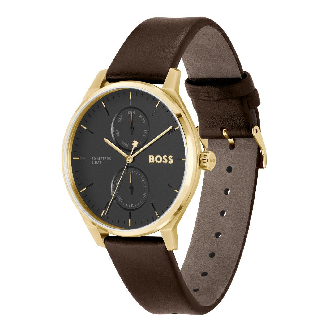 A Hugo Boss men's watch featuring a round gold-tone case, a black dial with gold hands and indices, and a dark brown leather strap, shown on a plain white background.
