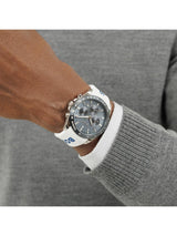 A close-up of a person's wrist wearing a BOOS chronograph watch with a white strap, silver case, and dark gray dial, styled with a white collared shirt and gray knit sweater.