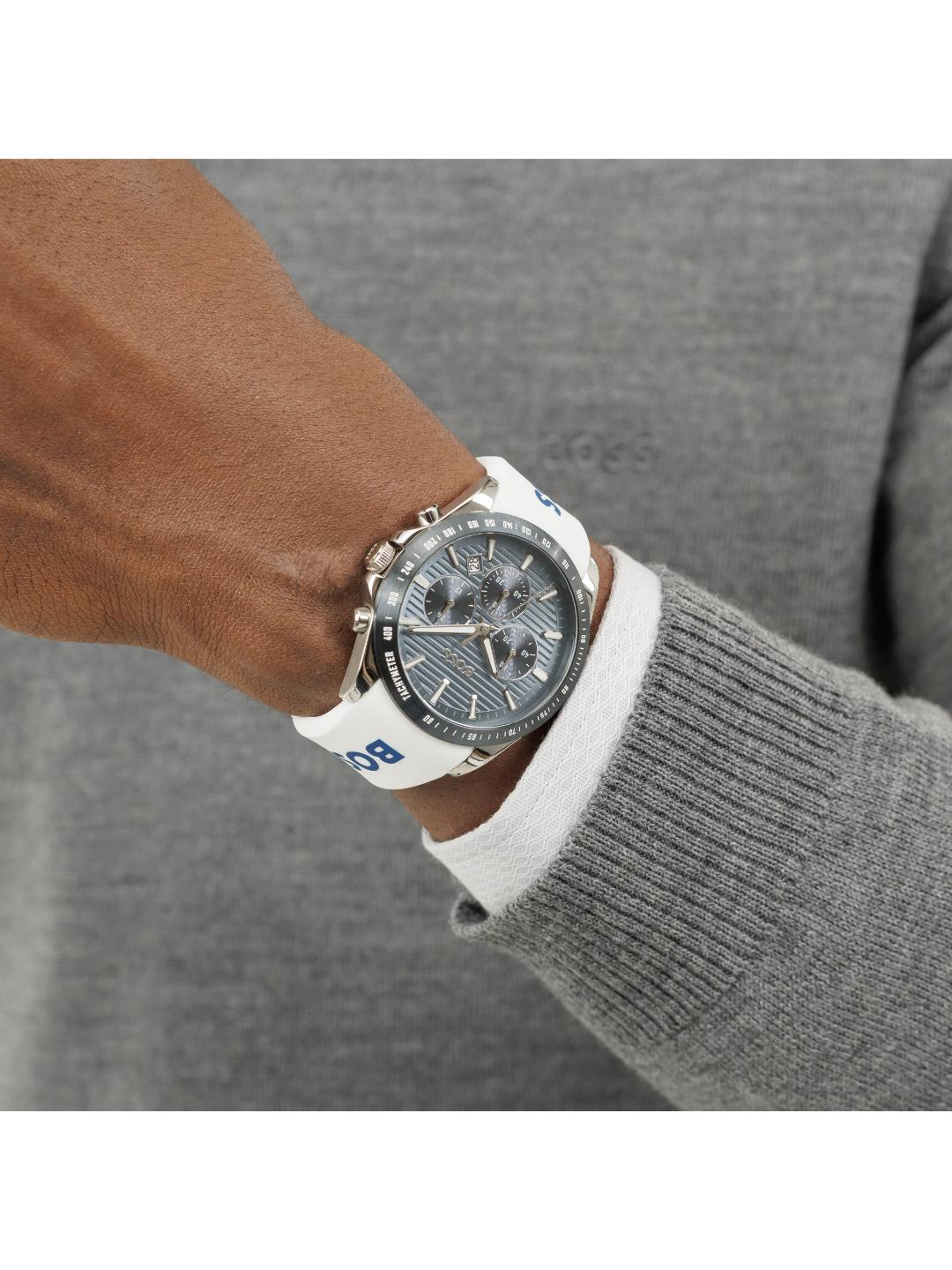 A close-up of a person's wrist wearing a BOOS chronograph watch with a white strap, silver case, and dark gray dial, styled with a white collared shirt and gray knit sweater.