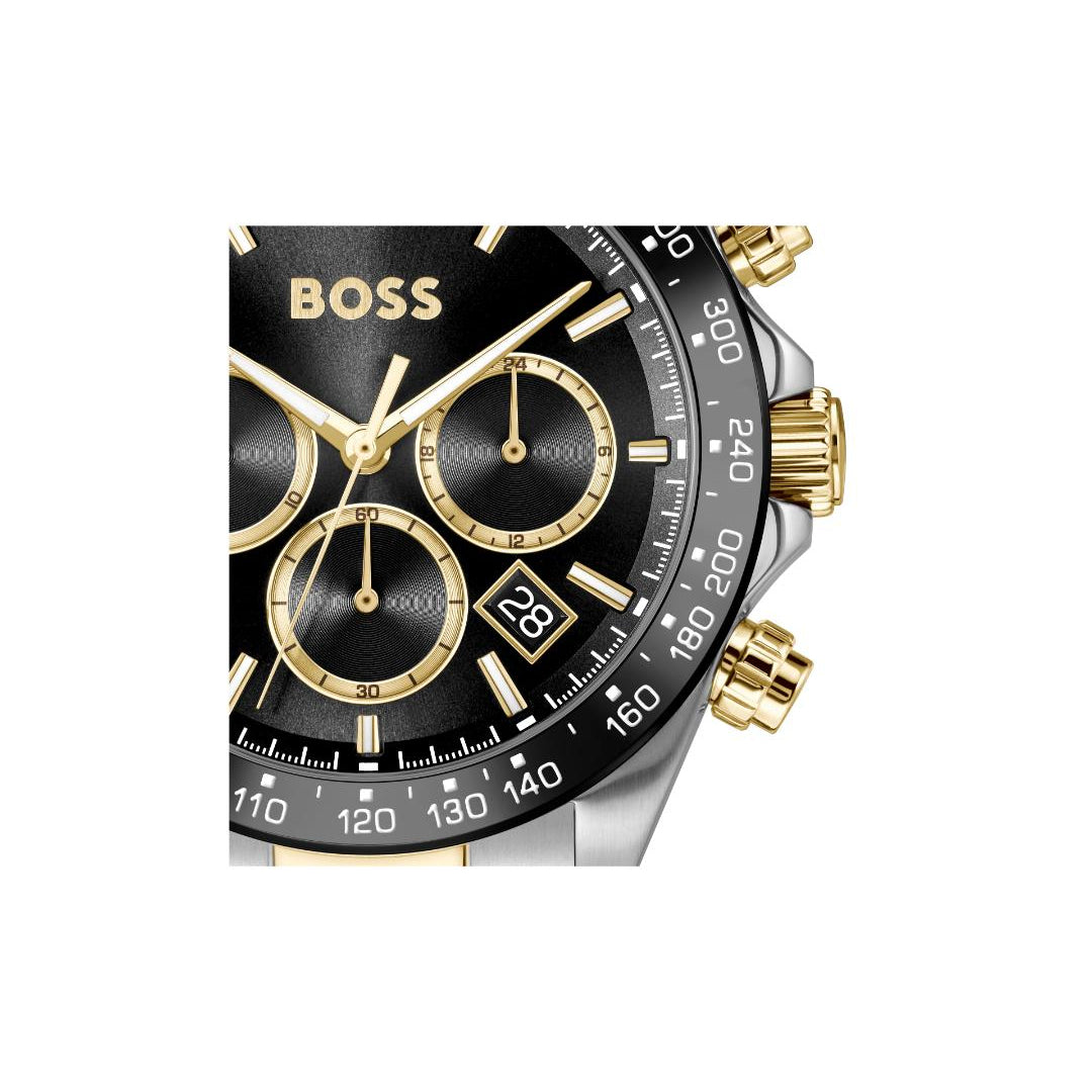 A Hugo Boss chronograph watch with a black dial, gold-tone bezel markings and hands, and a silver-tone stainless steel case with gold-tone pushers and lugs, shown on a plain white background.