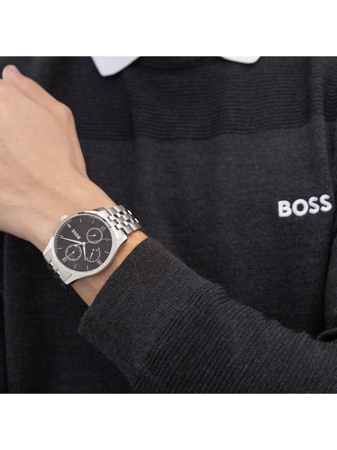 A silver-tone stainless steel watch with a black dial and multi-dial subdials, shown on a person's wrist wearing a dark gray BOSS sweater.