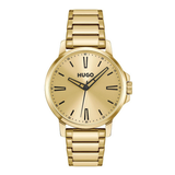 A gold-tone stainless steel wrist watch with a matching link bracelet, featuring a gold dial, black hour markers, and the HUGO brand name printed on the face, set against a plain white background.