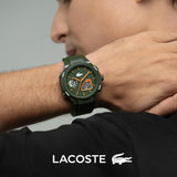 A man wearing a green Lacoste watch with orange accents on the dial and strap, shown in a close-up lifestyle shot with the Lacoste logo and crocodile emblem at the bottom.