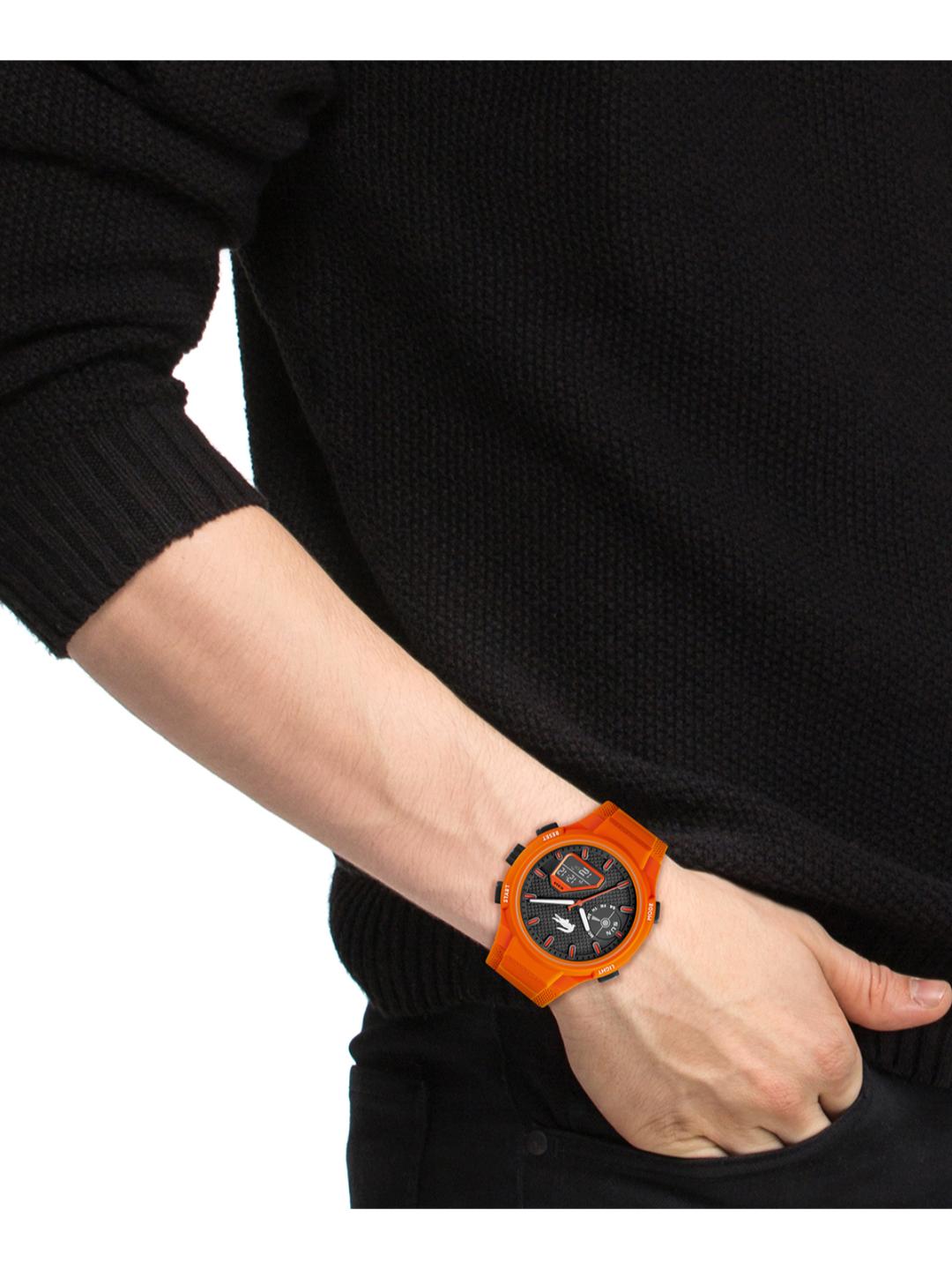 A close-up of a person's wrist wearing a bright orange analog watch with a black dial, set against a black knit sweater on a white background.