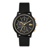 A black chronograph watch with a textured black strap, a black dial with gold-tone hands and indices, and the Lacoste crocodile logo at the 3 o'clock position.