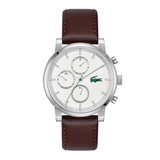 A luxury chronograph watch featuring a silver stainless steel case, a white dial with three sub-dials, and a brown leather strap with visible stitching. The green Lacoste crocodile logo is visible on the dial.