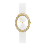 A Calvin Klein women's watch featuring an oval white dial, a gold-tone bezel encrusted with clear rhinestones, and a white strap, shown against a plain white background.