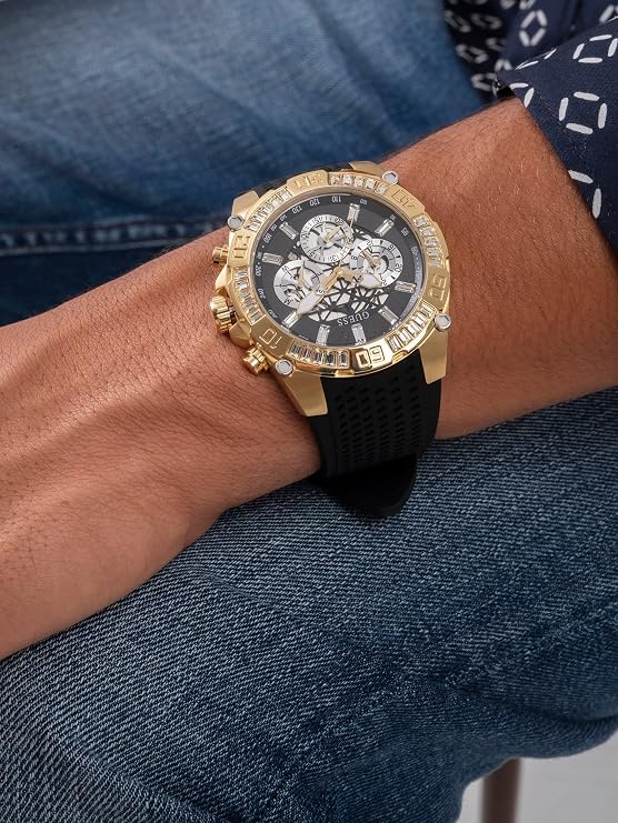 Gold wristwatch with black strap on a person's wrist wearing blue jeans.