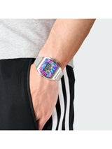 A close-up of a person's wrist wearing a silver-toned digital watch with a colorful, iridescent face displaying a pink and blue pattern.