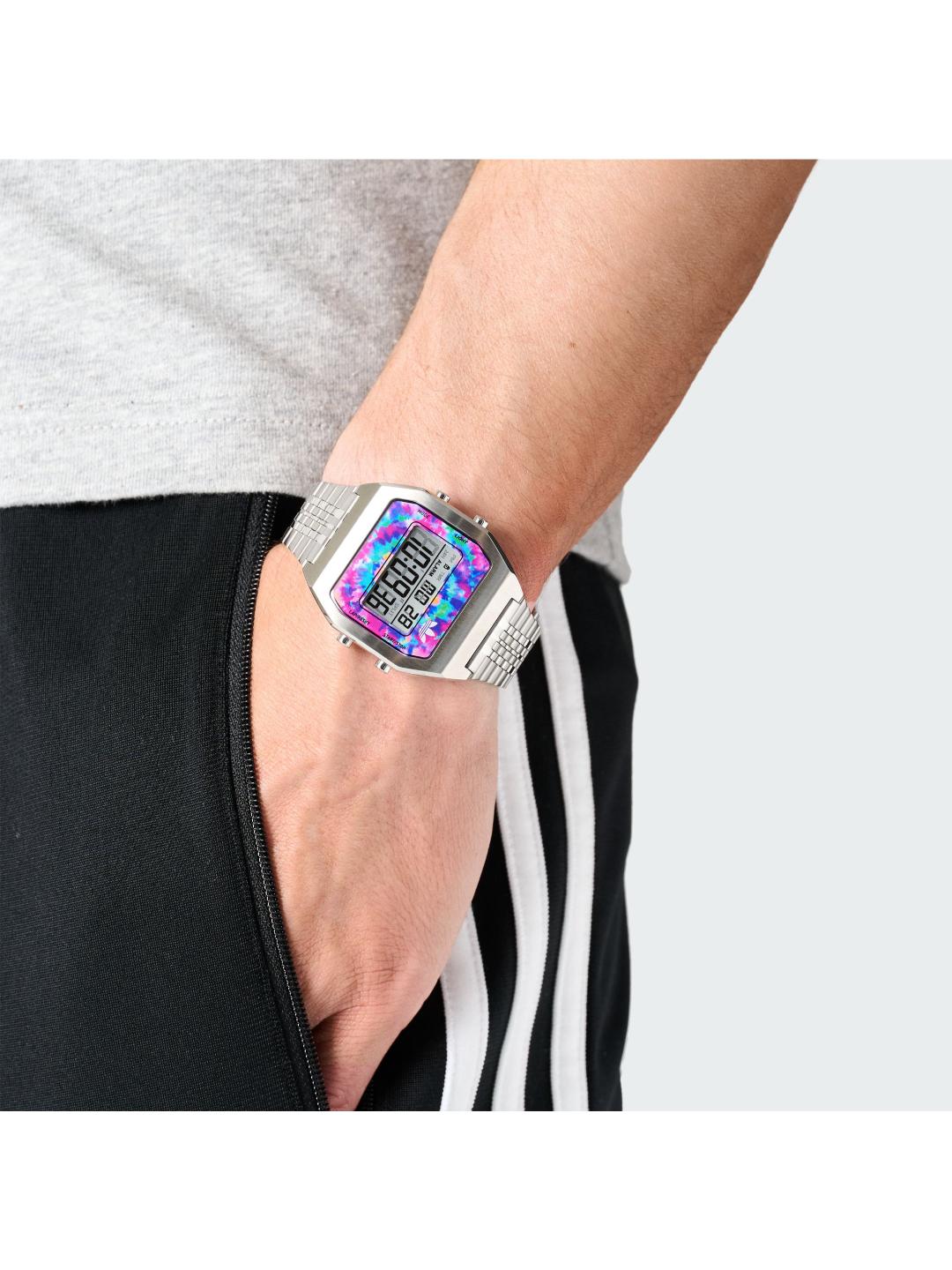 A close-up of a person's wrist wearing a silver-toned digital watch with a colorful, iridescent face displaying a pink and blue pattern.
