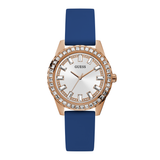 A Guess women's analog watch featuring a blue silicone strap, a rose gold case, a bezel encrusted with clear crystals, and a white dial with crystal hour markers.