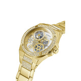 Gold-tone Guess women's watch with a crystal-studded bezel, skeletonized white dial showing gold gears, and a crystal-accented metal link bracelet on a white background.