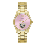 Gold-tone Guess watch with a pink dial, crystal-studded bezel, and a heart-shaped black-and-white pattern detail on the lower half of the face.