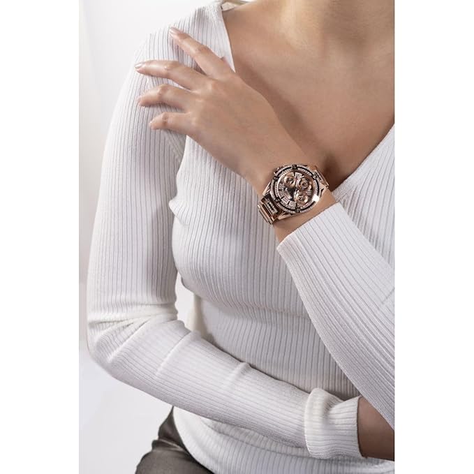 A close-up of a woman wearing a rose gold-toned watch with a metallic link bracelet and a patterned dial, paired with a white ribbed long-sleeve top.