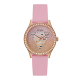 A Guess women's watch featuring a pink silicone strap, a rose gold case, and a glittery pink dial with a crystal-encrusted bezel and the signature geometric triangle logo.