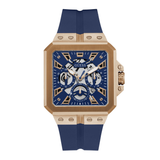 A GUESS men's watch featuring a square rose gold-tone case, a blue skeleton dial with gold and silver details, and a blue silicone strap, shown against a plain white background.