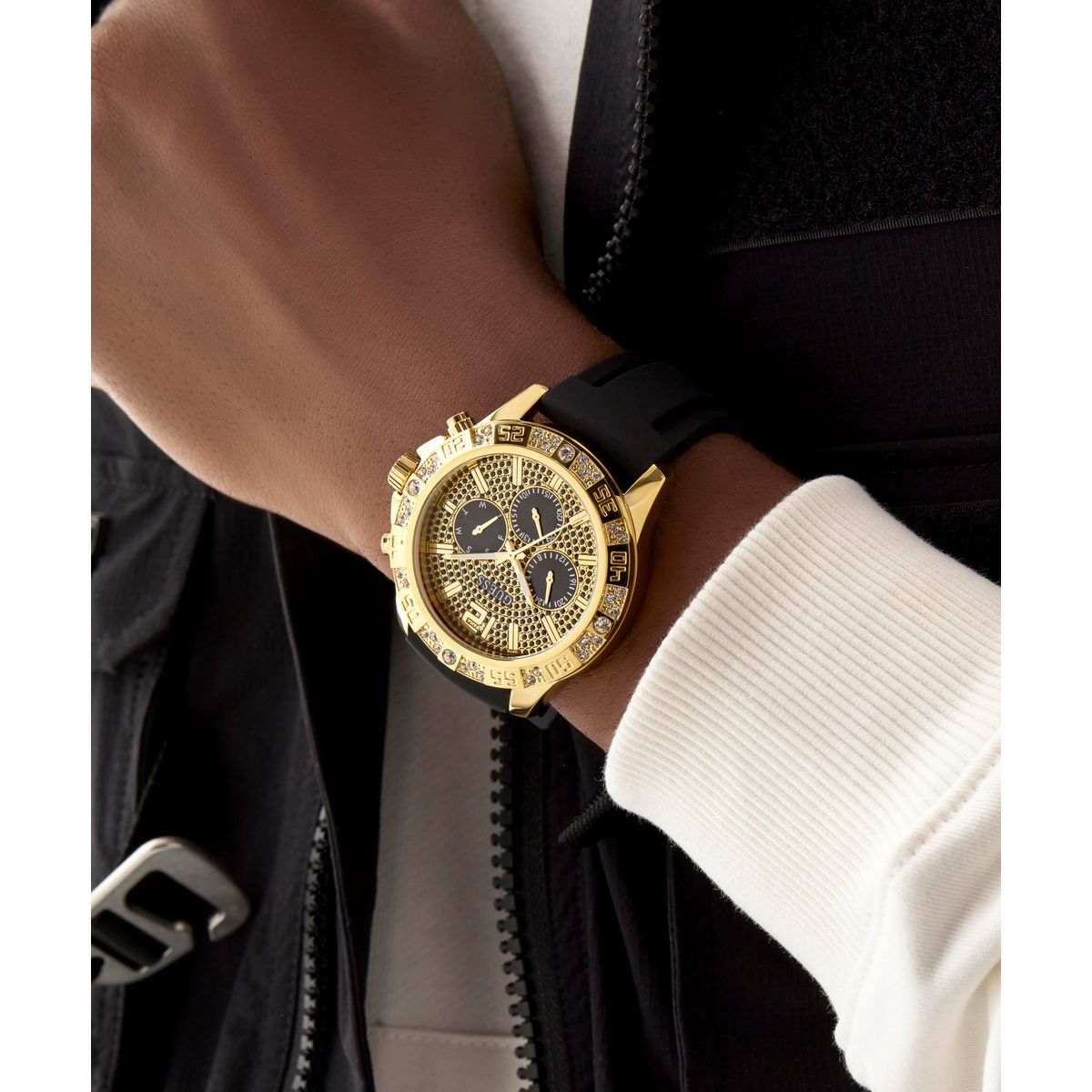 Gold watch with black strap on a wrist, wearing a black jacket and white shirt.