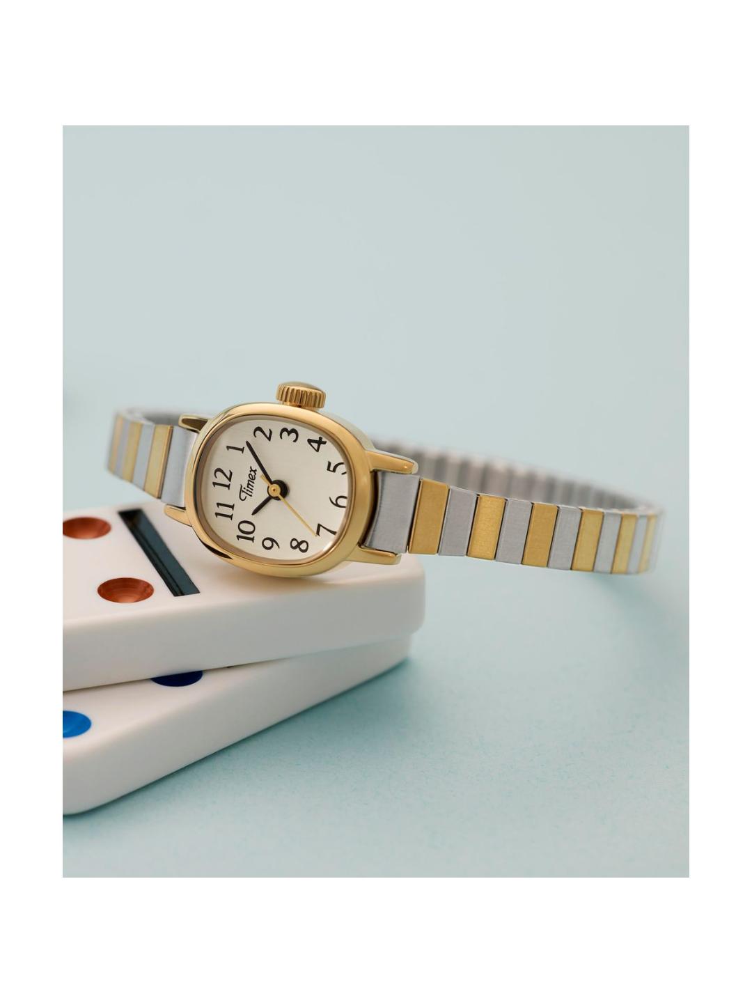 A women's two-tone watch with a gold case, white dial, and a silver-and-gold striped metal bracelet, resting on stacked white dice against a light blue background.