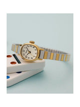 A women's two-tone watch with a gold case, white dial, and a silver-and-gold striped metal bracelet, resting on stacked white dice against a light blue background.