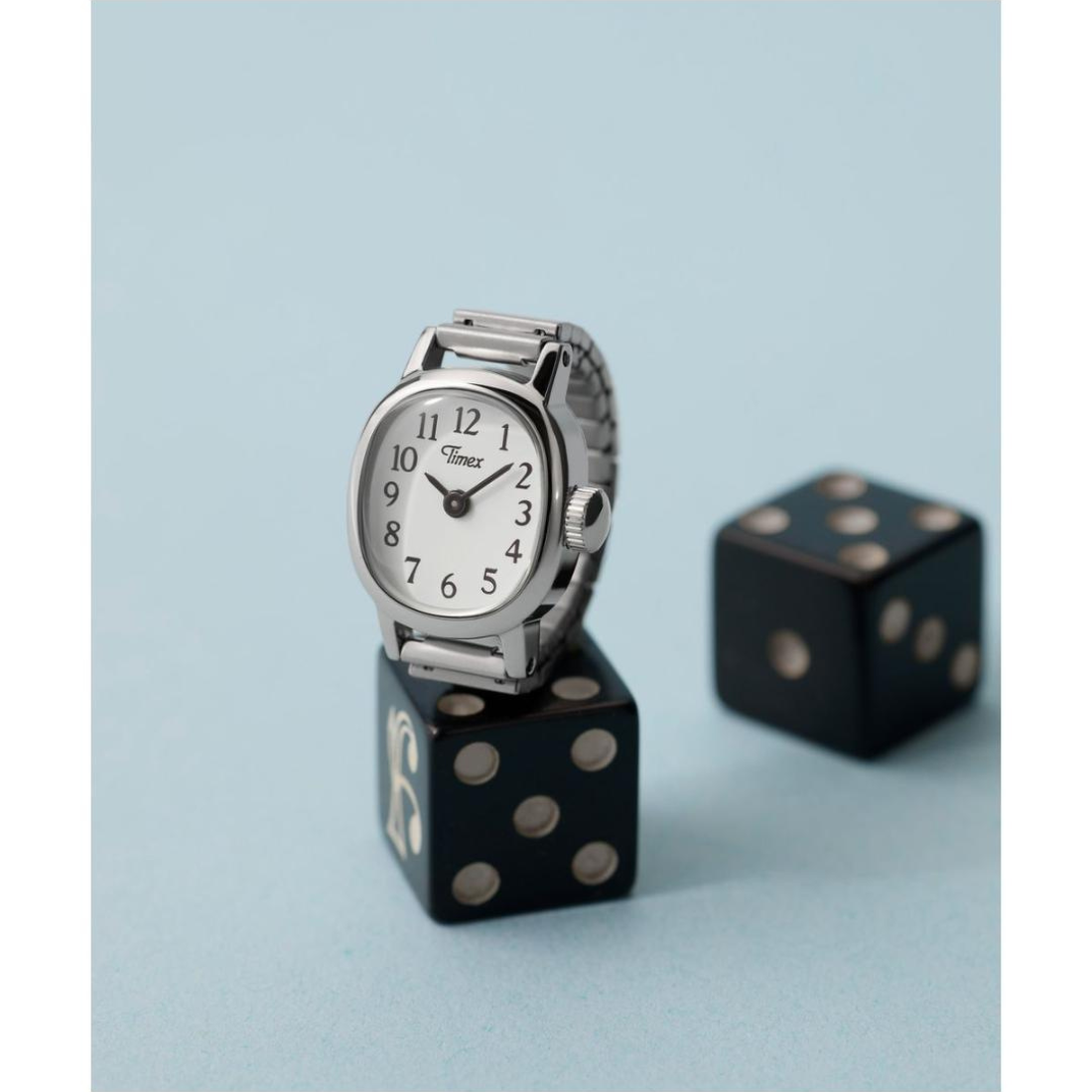 Silver Timex watch on a black die with another die in the background on a light blue background