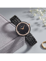 Black watch with rose gold accents on a gray surface with white flowers in the background