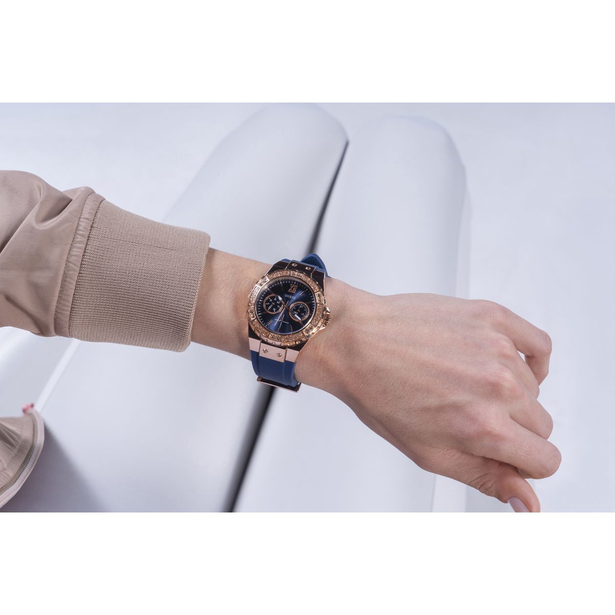 A close-up of a person's wrist wearing a luxury watch with a rose gold case, blue strap, and dark blue dial with gold details, set against a clean white background.