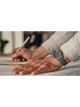 Person writing with a pen, wearing a watch on a blurred background